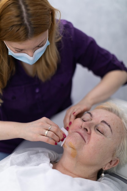 Una esteticista vestida con un uniforme púrpura limpia la cara de los clientes