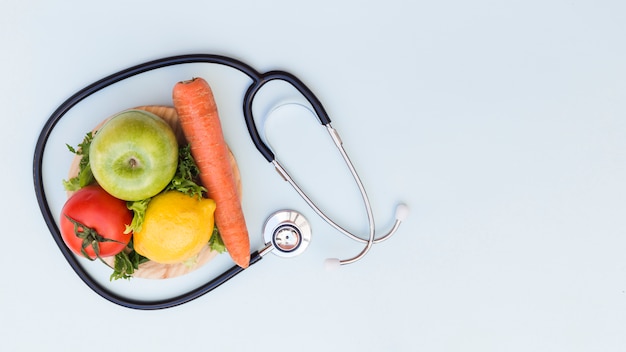 Foto estetoscopio alrededor de las verduras y frutas frescas sobre fondo blanco