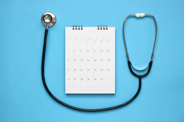 Estetoscópio com data de página de calendário na mesa azul, conceito médico de consulta médica