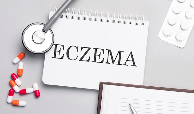 Estetoscópio, comprimidos e caderno com texto de eczema na mesa médica