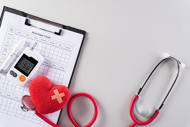 Estetoscópio, coração vermelho e kit de teste de açúcar no sangue na parede cinza.