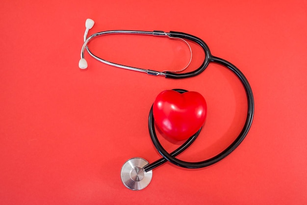 Estetoscópio, coração vermelho e lugar para texto em um fundo vermelho, plano leigo. Conceito de seguro saúde