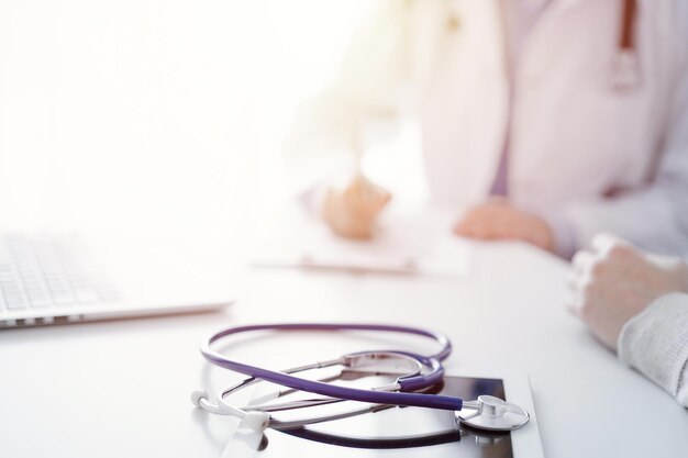 Estetoscópio deitado no tablet na frente de um médico e paciente ao fundo. Medicina, cuidados de saúde, conceito de mãos tranquilizadoras