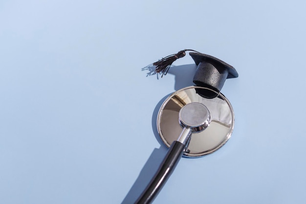 Estetoscópio e boné de formatura com sombra dura sobre fundo azul. Conceito de educação médica, close-up com espaço de cópia