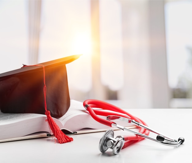 Foto estetoscópio e chapéu de pós-graduação com livro