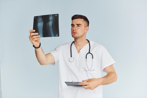 Con estetoscopio joven médico masculino en uniforme está en el interior contra el fondo blanco.