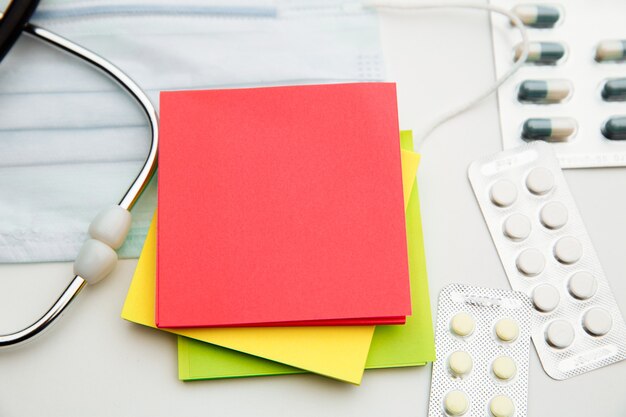 Estetoscopio, medicamentos, mascarilla y coloridas notas adhesivas para texto en blanco.