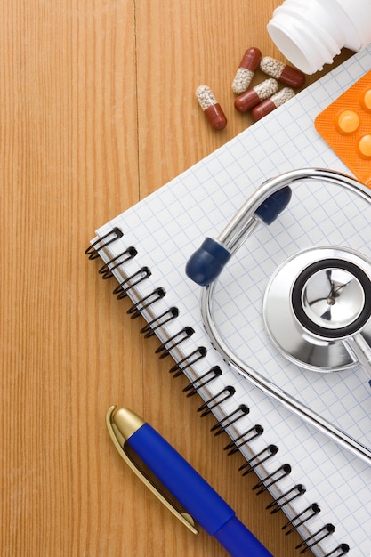 Foto estetoscópio médico com comprimidos e caderno em madeira