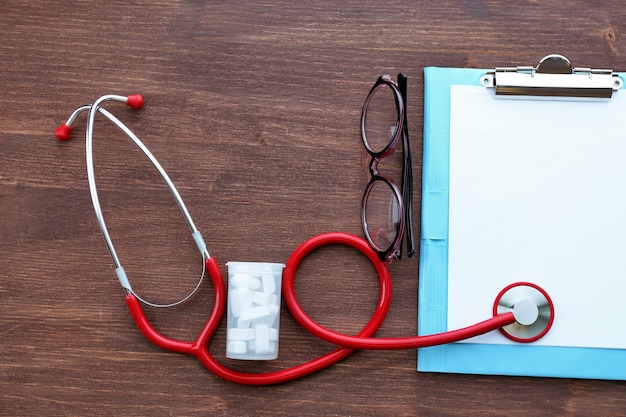 Estetoscópio médico com prancheta e comprimidos na mesa de madeira fechar