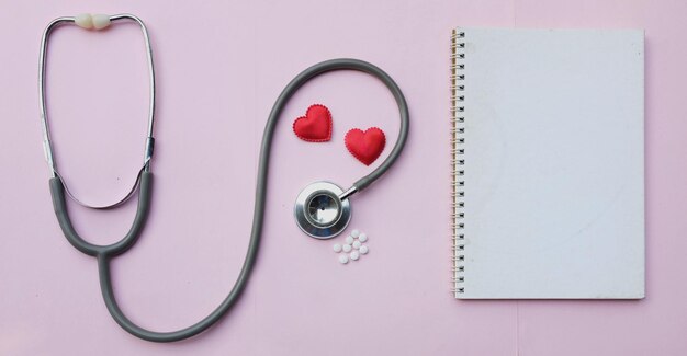 Foto estetoscopio médico y corazones decorativos cuaderno blanco en un fondo pastel rosa de color equipo médico en un escritorio de la oficina de un médico concepto minimalista de la tendencia del día de san valentín
