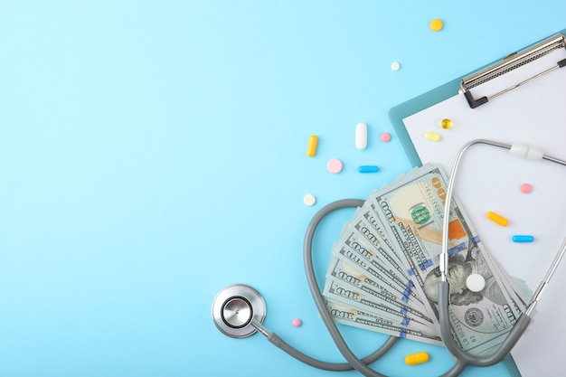 Estetoscópio médico e dinheiro em plano de fundo colorido vista superior