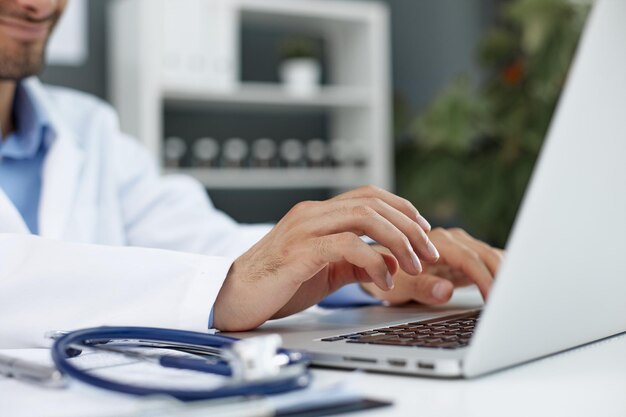 Foto estetoscopio y médico de fondo usando computadora portátil en el escritorio en la clínica trabajando en la computadora en la oficina de la habitación