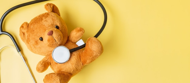 Estetoscopio con muñeca Bear sobre fondo amarillo para apoyar la vida y la enfermedad de los niños. Septiembre mes de concientización sobre el cáncer infantil, concepto de seguro de vida y salud