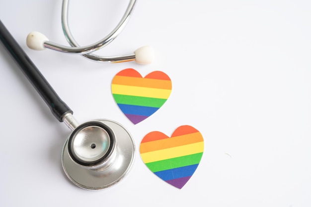 Estetoscopio negro con el corazón de la bandera del arco iris en el símbolo de fondo blanco del mes del orgullo LGBT