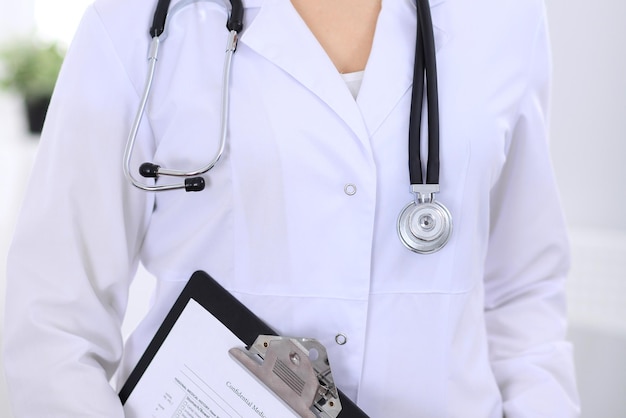 Estetoscopio en el pecho de una doctora en el consultorio del hospital. Primer plano de las manos de un médico desconocido. Concepto de medicina y atención de la salud.