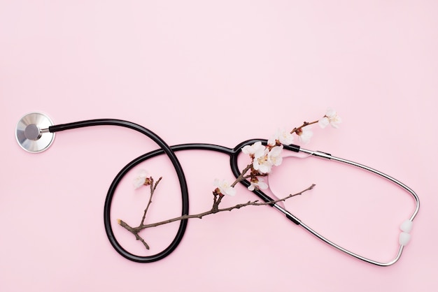 Foto estetoscópio plano leigo com ramo de primavera florescendo em rosa