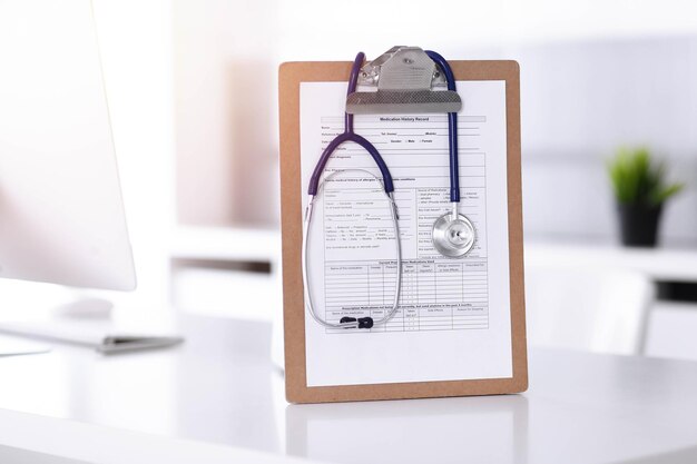 Foto el estetoscopio y el portapapeles con registros de historial de medicamentos están sobre la mesa en el lugar de trabajo del médico soleado. concepto de medicina.