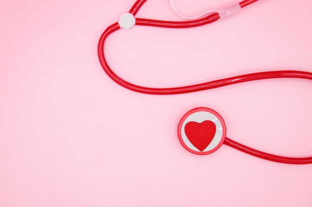 Foto estetoscopio rojo con un corazón sobre fondo rosa