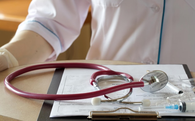 Estetoscópio sobre a mesa de um médico. Resultados de análises de sangue em segundo plano. Fechar-se