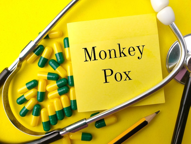 Estetoscópiopencilpill e nota adesiva com a palavra MONKEY POX em fundo amarelo