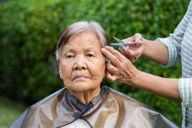 Estilista de cabello cortando el cabello gris de la mujer mayor