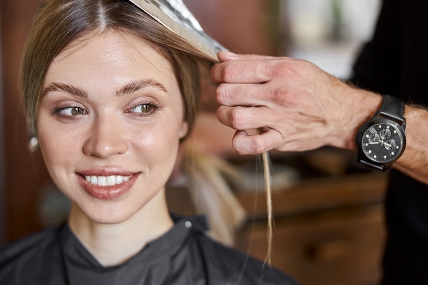 Estilista confiante está tingindo o cabelo de uma cliente loira, branca