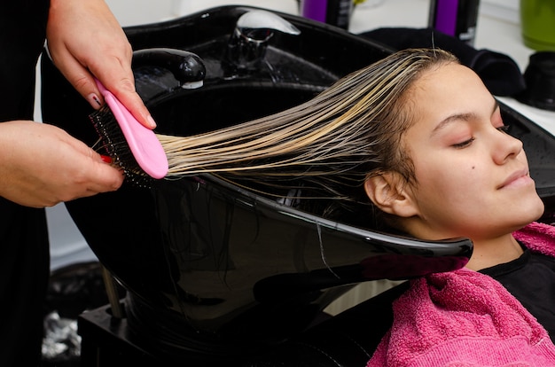 Estilista de cabelo, aplicar a máscara de cabelo e pentear clientes molhar o cabelo com escova em uma pia preta.