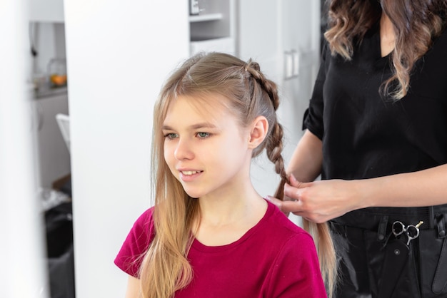 Estilista de cabelo tece trança para menina pré-adolescente no salão de beleza