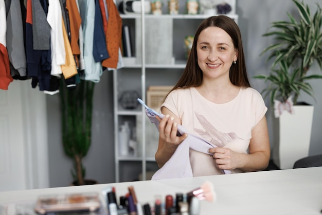 Foto estilista de moda caucasiana usando telefone celular recebendo ordem de compra e mostrando roupas