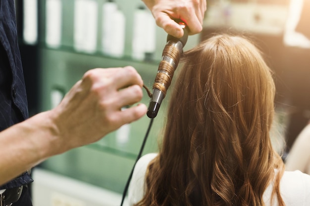 Estilista haciendo hermosos rizos con rizador en el cabello del cliente. Creación de peinado de noche de lujo con rizos, espacio de copia