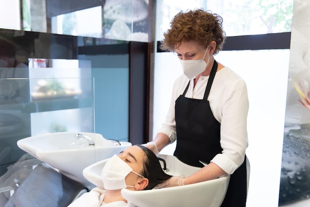 Un estilista le lava el cabello a un paciente adolescente que usa una máscara facial