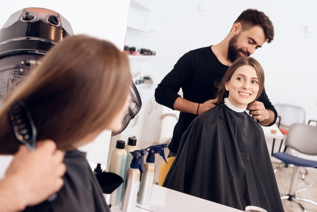 El estilista del peluquero está peinando a la mujer joven con el pelo marrón.