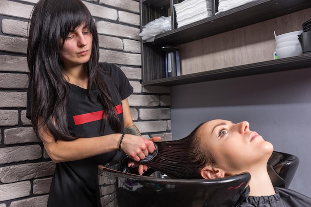 Estilista profesional femenino peinando el cabello de la joven y bella mujer en el lavabo de lavado en el salón de belleza