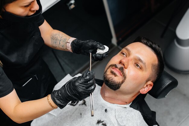 Un estilista profesional en una peluquería con estilo moderno afeita y corta el cabello de un joven. Salón de belleza, peluquería.