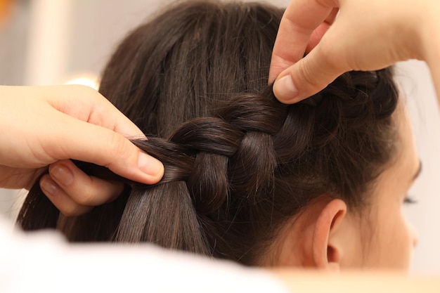 Estilista profesional trenzando el cabello del cliente en un primer plano de fondo borroso