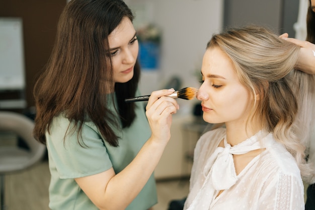 Estilista profissional e maquiador fazendo maquiagem e penteado para mulher jovem