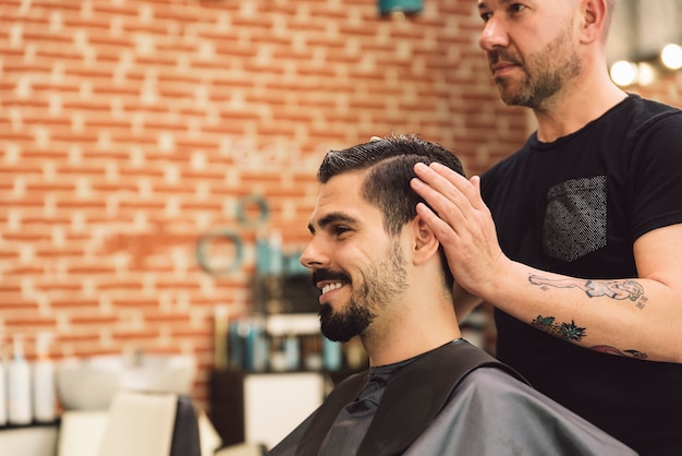 Estilista que corte de pelo de los hombres a un hombre atractivo en el salón de belleza.