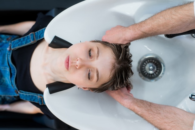 Estilista en el trabajo: peluquera lavando el cabello a la clienta adolescente antes de peinarse