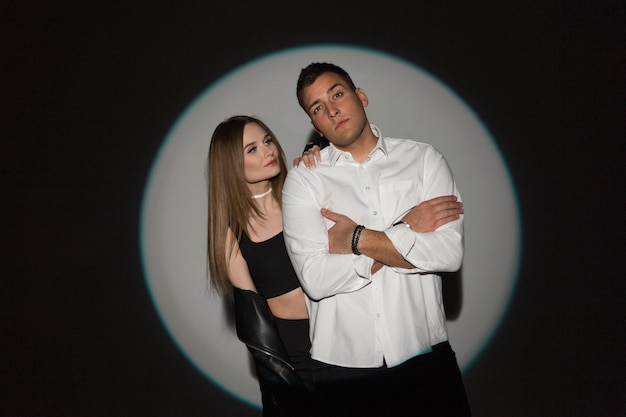 Estilizando um belo casal jovem mulher bonita e homem bonito em roupas casuais da moda em um fundo escuro no estúdio com uma luz circular criativa