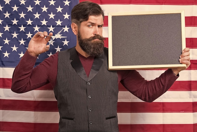 Estilo americano Estilista de peluquero americano o peluquero Fondo de bandera americana Hombre con barba y bigote con bandera americana sostiene tijeras y espacio de copia de pizarra 4 de julio Horas felices