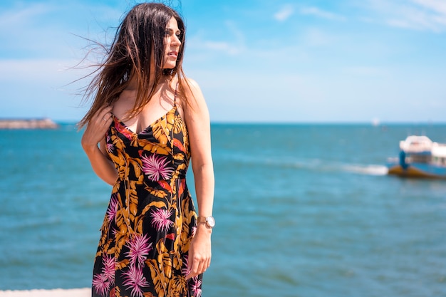 Estilo callejero, retrato de una joven morena delgada con un hermoso vestido floral y sombrero mirando a la derecha