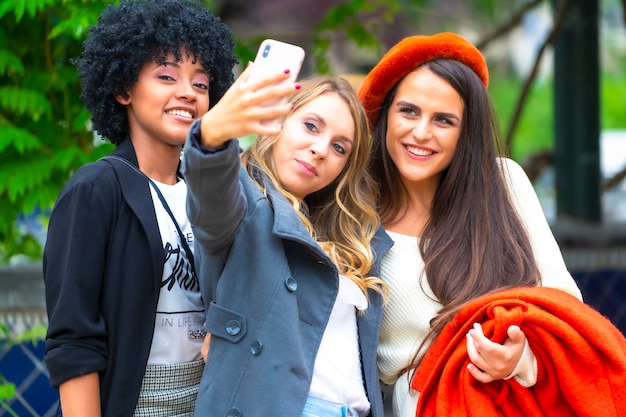 Estilo callejero. Tres amigos tomando una selfie en la ciudad, una rubia, una morena y una chica latina con cabello afro