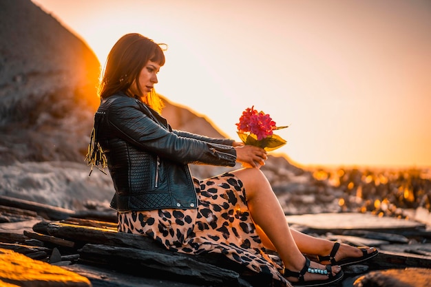 Estilo callejero de verano en una playa junto a las rocas de una joven morena caucásica con un vestido de leopardo junto al mar Playa Sakoneta en la ciudad de Deba País Vasco Mirando a la derecha