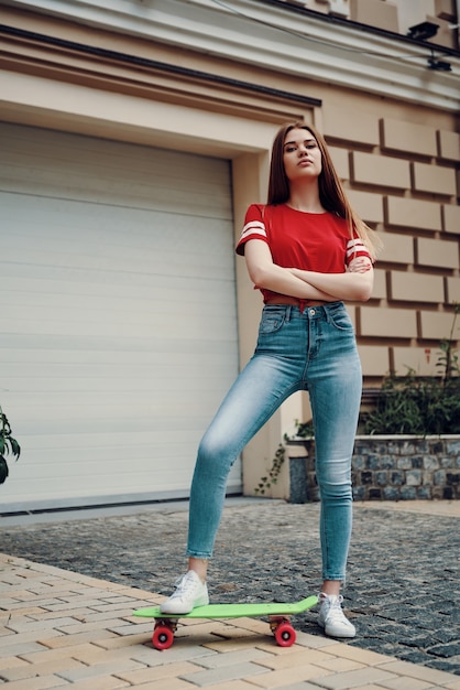 Estilo de ciudad. Longitud total de mujer joven atractiva manteniendo los brazos cruzados mientras está de pie al aire libre