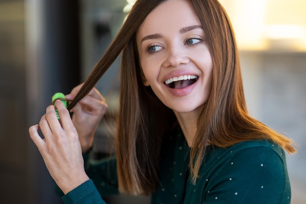 Estilo de cabelo. Mulher jovem sorridente demonstrando dicas de penteado