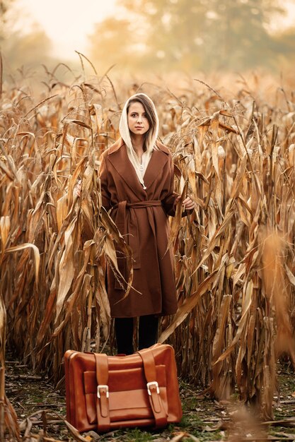 Estilo de mulher de casaco com mala no campo de milho na temporada de outono