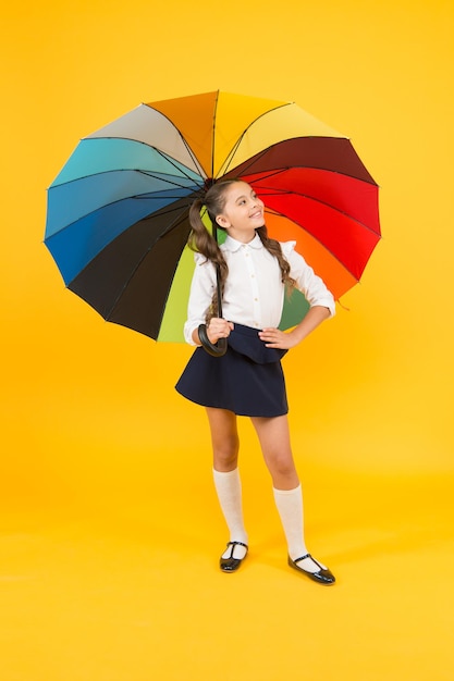 Estilo de outono Pequena menina segurando guarda-chuva colorido para o clima de outono em fundo amarelo Pequeno aluno indo para a escola no dia de outono ou 1 de setembro De volta à escola no outono