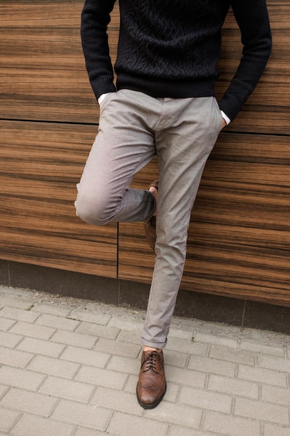 Foto estilo de roupas casuais de moda de negócios. homem irreconhecível relaxado, apoiando-se na parede de textura de madeira ao ar livre