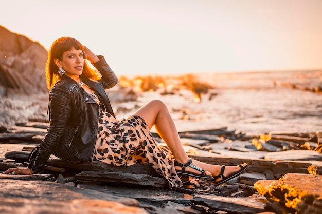 Estilo de rua de verão em uma praia ao lado de rochas de uma jovem morena caucasiana em um vestido de leopardo à beira-mar Praia de Sakoneta na cidade de Deba País Basco Olhando para a direita