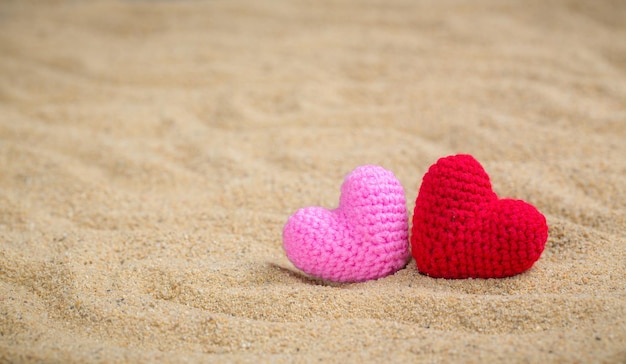 Estilo de verão com tricô de coração vermelho e rosa em um fundo de areia do mar para adicionar texto Contexto amor conceito de cartão de saudação dos namorados